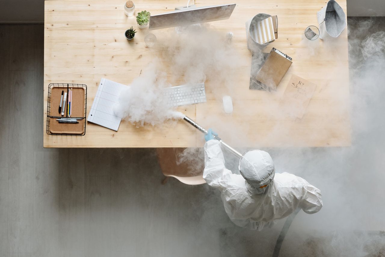 hero-img An individual disinfects a workspace using fumigation, wearing full protective gear for safety.